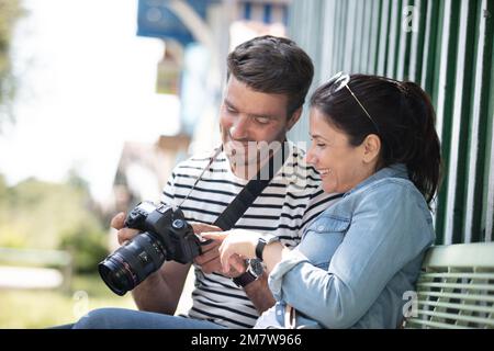 couple of tourists reviewing photos on camera sitting on bench Stock Photo