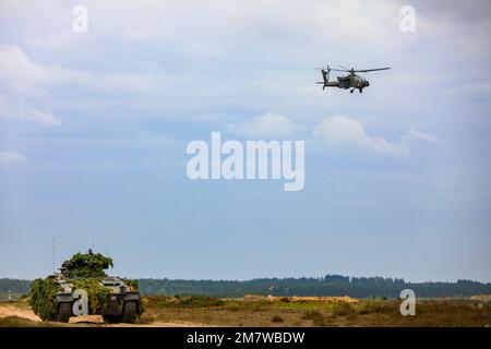 A U.S. Army AH-64E Apache guardian assigned to Task Force Palehorse of the 7th Squadron, 17th Cavalry Regiment, 1st Air Cavalry Brigade, flies overhead a German armored personnel carrier during a multinational field training exercise during Defender Europe 2022, Drawsko Pomorskie, Poland, May 15, 2022. Defender Europe 22 is a series of U.S. Army Europe and Africa multinational training exercises in Eastern Europe. The exercise demonstrates U.S. Army Europe and Africa’s ability to conduct large-scale ground combat operations across multiple theaters supporting NATO. Stock Photo