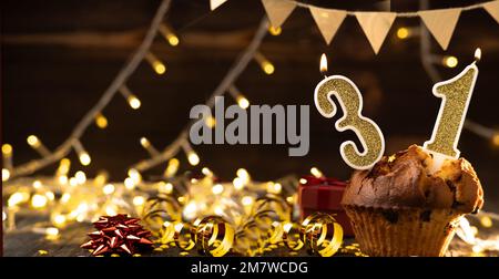 Number 31 gold burning candle in a cupcake against celebration wooden background with lights. Birthday cupcake. Copy space. Banner Stock Photo