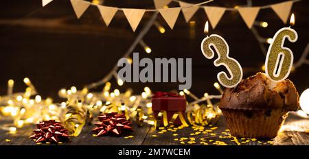 Number 36 birthday celebration candle in cupcake against lights and wooden background. Copy space. Banner Stock Photo