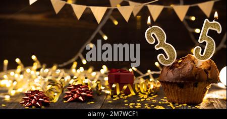 Number 35 birthday celebration candle in cupcake against lights and wooden background. Copy space. Banner Stock Photo