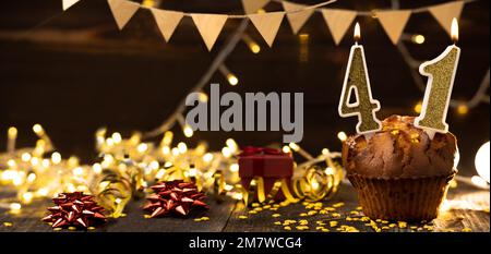 Number 41 birthday celebration candle in cupcake against lights and wooden background. Copy space. Banner Stock Photo