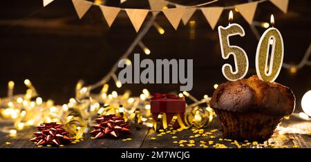 Number 50 golden festive burning candles in a cake, wooden holiday background. fifty years of birth. the concept of celebrating a birthday, anniversar Stock Photo