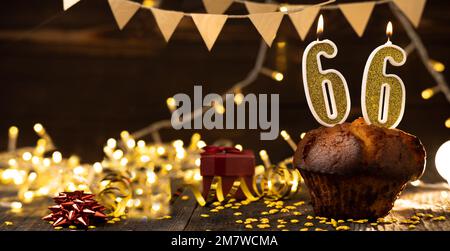 Number 66 golden festive burning candles in cake, wooden holiday background. sixty-six years of birth. the concept of celebrating a birthday, annivers Stock Photo