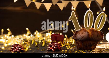 Number 100 golden festive burning candles in a cake, wooden holiday background. hundred years since the birth. the concept of celebrating a birthday, Stock Photo