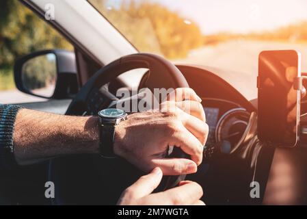 Man with both hands on steering wheel driving at sunset Stock Photo