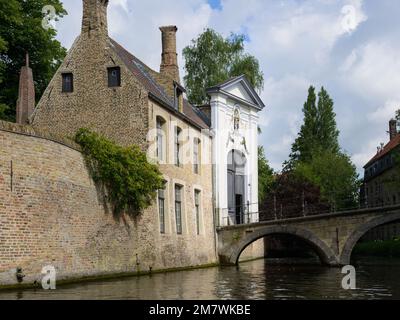 Bruges, Belgium-July 4, 2022: An old house at a canal with a bridge, daylight, trees Stock Photo