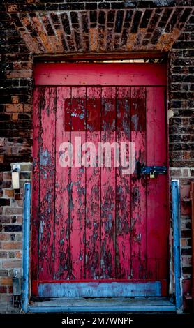 Weatherworn red gate with blue rails in a brick wall Gate had a new padlock keeping it closed. Stock Photo