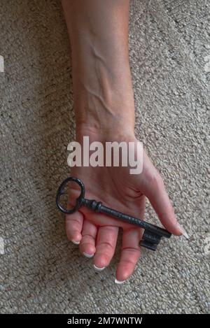 close up of young woman's hand holding an old key, laying on a carpet. Mystery thriller book cover style. Stock Photo