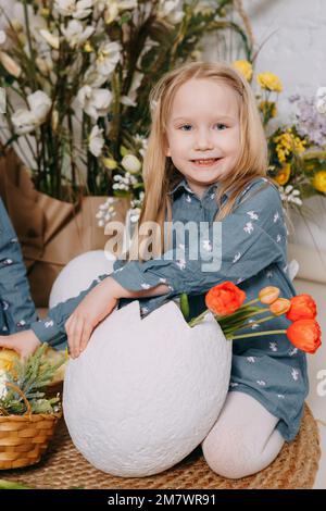 Two girls in a beautiful Easter photo zone with flowers, eggs, chickens and Easter bunnies. Happy Easter holiday Stock Photo