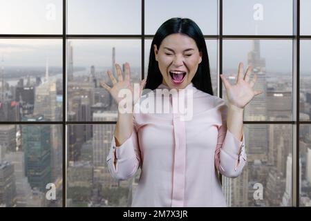 Portrait of young asian woman screaming out loud. Checkered windows and cityscape background. Stock Photo