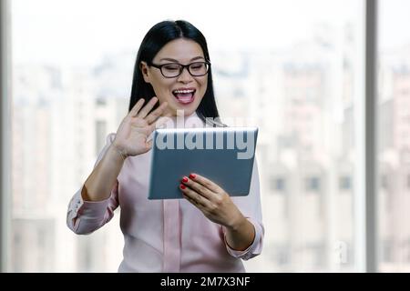Young asian businesswoman to someone via tablet pc. Blurred windows backgorund. Stock Photo