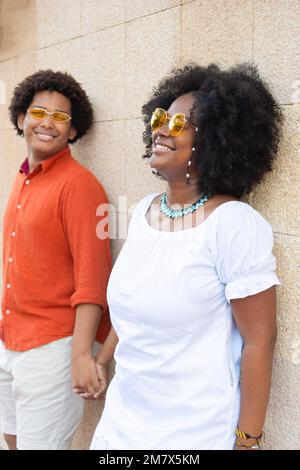ethnic couple looking sideways against a brick wall. Stock Photo