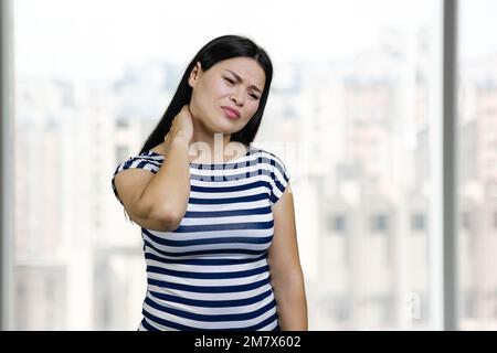 Portrait of asian woman suffering from neck pain. Office windows background. Stock Photo