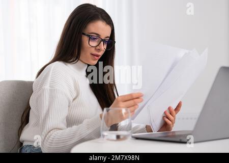 Business woman in white shirt using laptop computer and checking documents. Stock Photo
