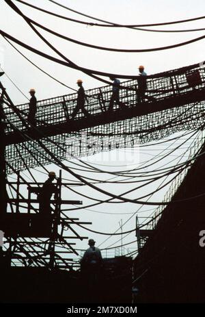 Shipyard workers cross the gangplank to the dry docked guided missile destroyer USS CLAUDE V. RICKETTS (DDG-5). They are silhouetted within a web of power line connected between the ship and the yard. Base: Norfolk Naval Shipyard State: Virginia (VA) Country: United States Of America (USA) Stock Photo