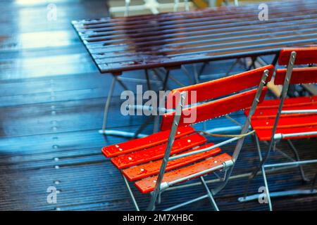 Outdoor terrace chairs and tables in raindrops . Street terrace in rainy day . Water drops on wooden surface Stock Photo