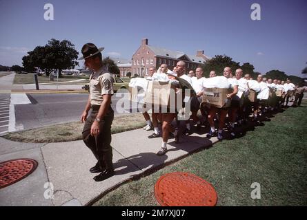 Aviation Officer Candidates laden with boxes of uniforms and supplies struggle to keep up with their Marine gunnery sergeant drill instructor during the first of 14 weeks of training. Base: Naval Air Station, Pensacola State: Florida (FL) Country: United States Of America (USA) Stock Photo