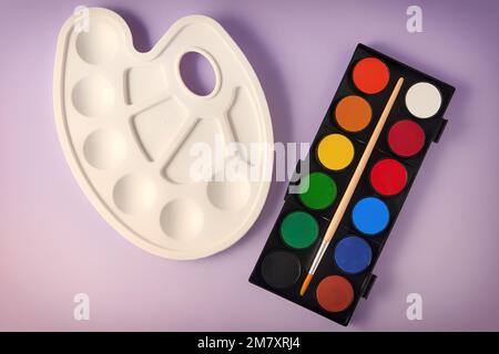 Brand new watercolor paints, brush and plastic palette on a purple background. Drawing, arts and hobby backgrounds and templates Stock Photo