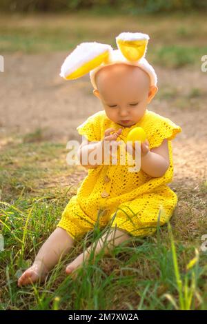 Cute little baby with bunny ears on Easter day. The girl hunts for Easter eggs on the lawn. Girl with Easter eggs in the rays of the setting sun. Stock Photo