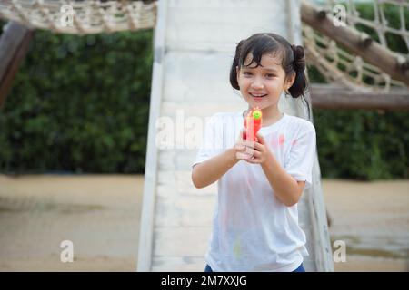 Happy child girl has fun playing sliding and shooting water gun on outdoor playground on hot summer day outdoors. Stock Photo