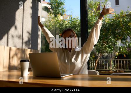 Exhausted businesswoman stretching with arms raised while working in coworking office. Stock Photo