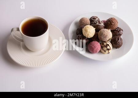 photo assorted chocolates lying in a round white plate next to a cup of coffee on a saucer Stock Photo
