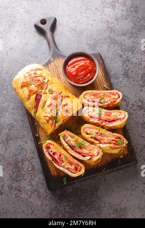 Freshly baked hot pizza stromboli roll with sausage and cheese close-up on a wooden board on the table. Vertical top view from above Stock Photo