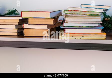 Stacks of books in colorful covers on table near white wall Stock Photo