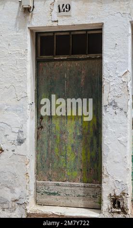 An old distressed green painted door in a white wall on the Spanish Island of Menorca Stock Photo