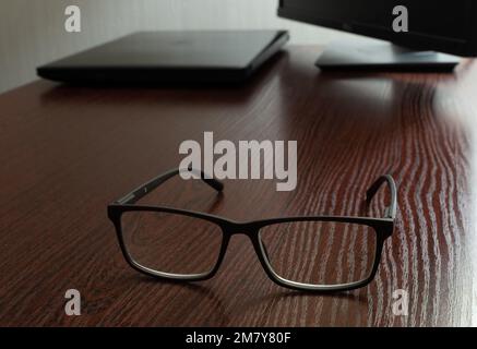 Stylish glasses on wooden office table close-up on blurred background of laptop and display Stock Photo