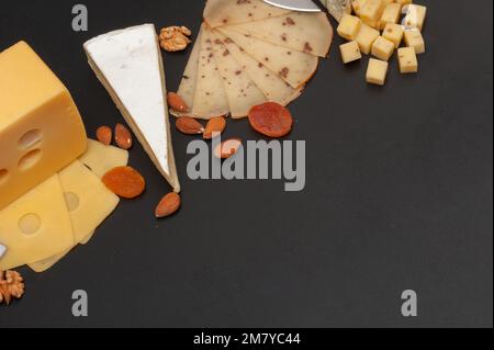 Different types of cheese on a wooden board decorated with grapes, dried apricots and nuts Stock Photo