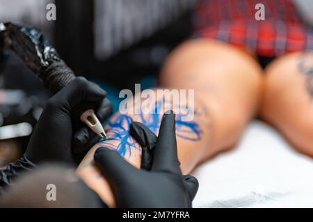 A closeup of a tattoo artist doing a tattoo art on a woman's leg at the salon Stock Photo