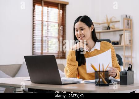 Beautiful young smiling asian businesswoman working on laptop and drinking coffee, Asia businesswoman working document finance and calculator in her Stock Photo