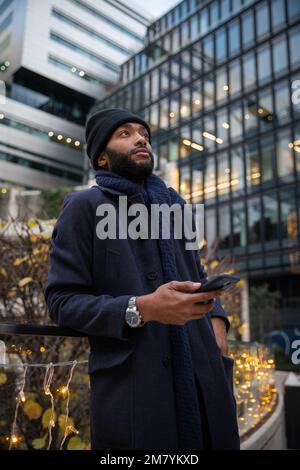 African businessman looks up with a thoughtful expression and holds his phone Stock Photo