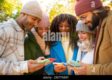 Group of young multi-ethnic friends using cell phones outdoors. People addicted to technology. Stock Photo