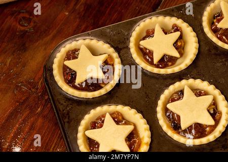 Closeup of star topped mince pies in a dark metal bun tin before baking. Stock Photo