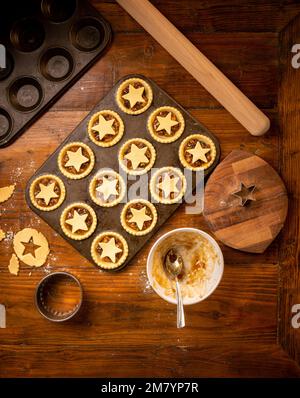 Flat lay of metal bun tin containing star topped mince pies ready for baking. Christmas baking. Stock Photo