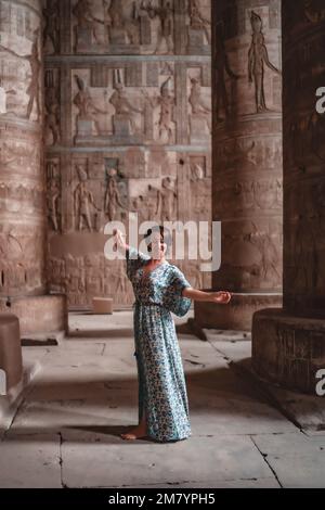 A vertical shot of a young woman in a summer dress posing in an ancient Egyptian temple. Stock Photo