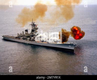 A starboard bow view of the battleship USS NEW JERSEY (BB 62) as its 16-inch guns are fired to port during tests on the Pacific Missile Test Center (PMTC) range. Country: Pacific Ocean (POC) Stock Photo