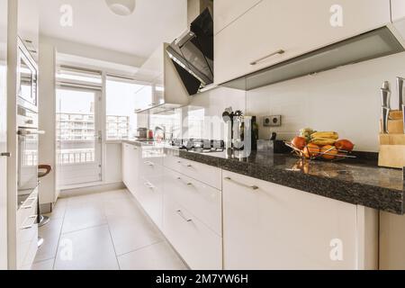 a kitchen with white cabinets and black counter tops in front of the window, looking out onto an outside patio Stock Photo