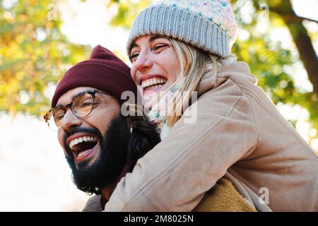 Close up portrait of lovely couple hugging. Young bearded man with glasses giving his blonde cute girlfriend a piggyback ride. High quality photo Stock Photo