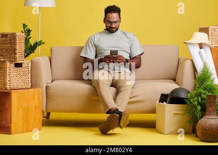 Man sitting on sofa and texting friends and colleagues Stock Photo