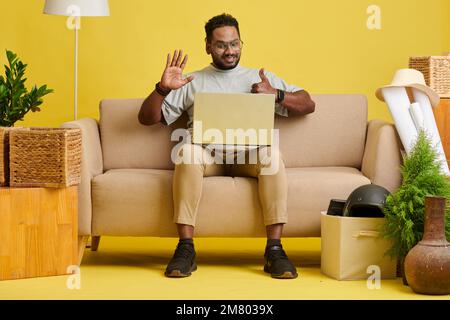 Happy excited businessman showing thumbs-up and waving with hand when greeting colleagues at online meeting Stock Photo