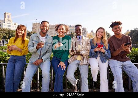 Multiracial group of friends using mobile phone and looking at camera smiling. Stock Photo