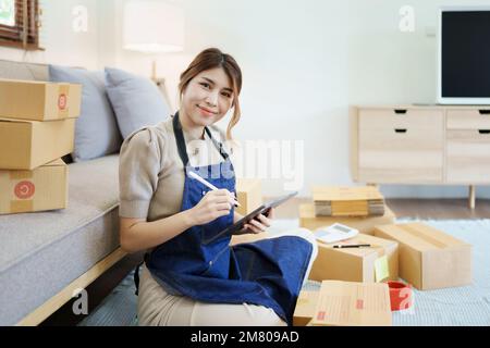 Starting small business entrepreneur of independent young Asian woman online seller is using smart phone and taking orders to pack products for Stock Photo