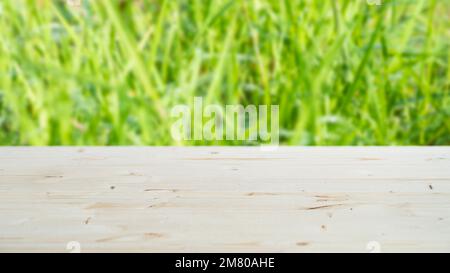A light wooden tabletop with copy space for installing a product or layout on a background with green grass in blur. Horizontal orientation. Stock Photo