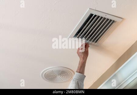 Handyman adjusting HVAC ceiling air vent. Air flow adjustment for overhead home heat and air conditioning ventilation duct. Stock Photo