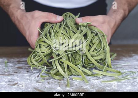 Fresh pasta. Homemade Italian raw pasta fettuccine with spinach in the hands of the chef on the background of the kitchen. High quality photo Stock Photo