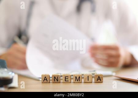 Word anemia on table and blurred doctor filling out medical paperwork in background. Stock Photo